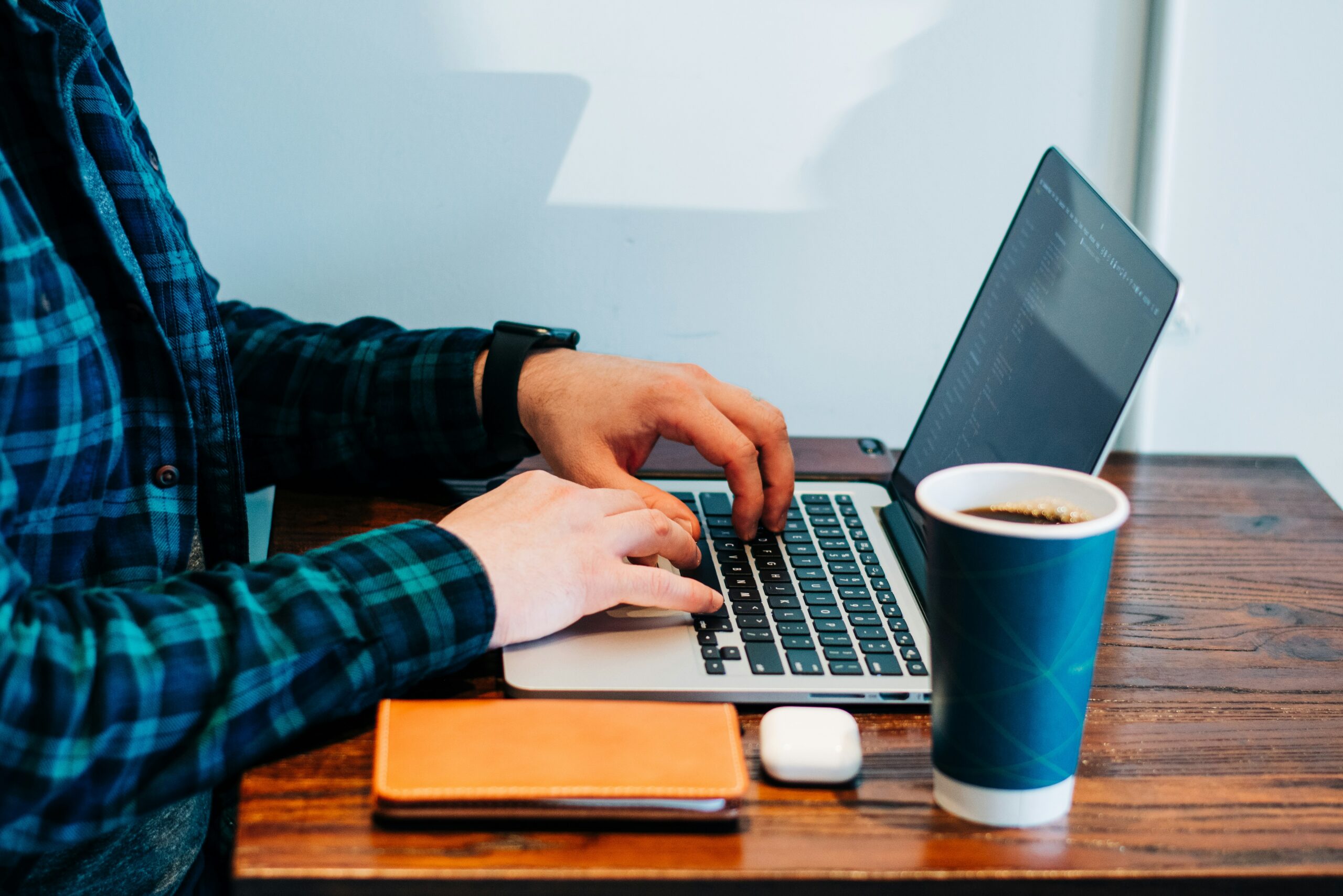 Mensch vor einem Computer, daneben ein Kaffeebecher